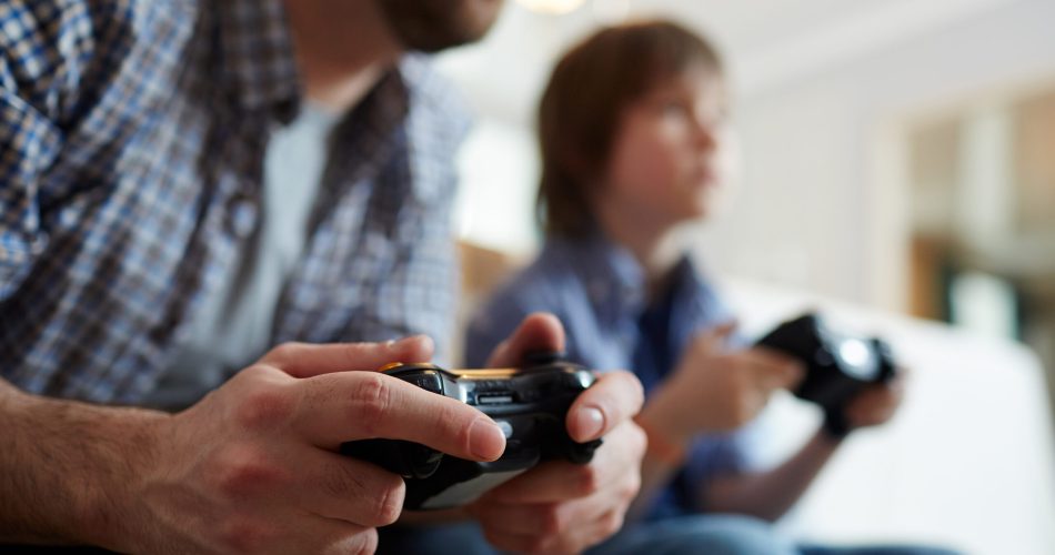 Young man with joystick playing video game on background of his son