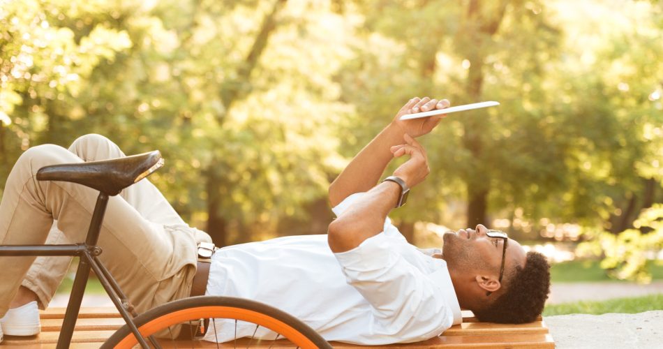 Photo of young african man early morning with bicycle outdoors. Looking aside using tablet computer.