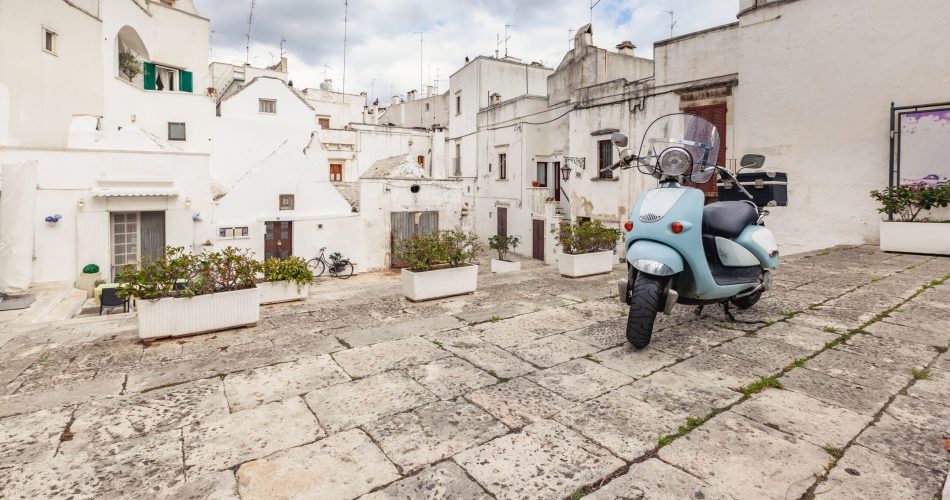 Wonderful view of the empty streets of old town Martina Franca with a beautiful houses painted in white among greenery. Classic blue moped on the background of an anient buildings. Nice day in a tourist town, Apulia, Italy.
