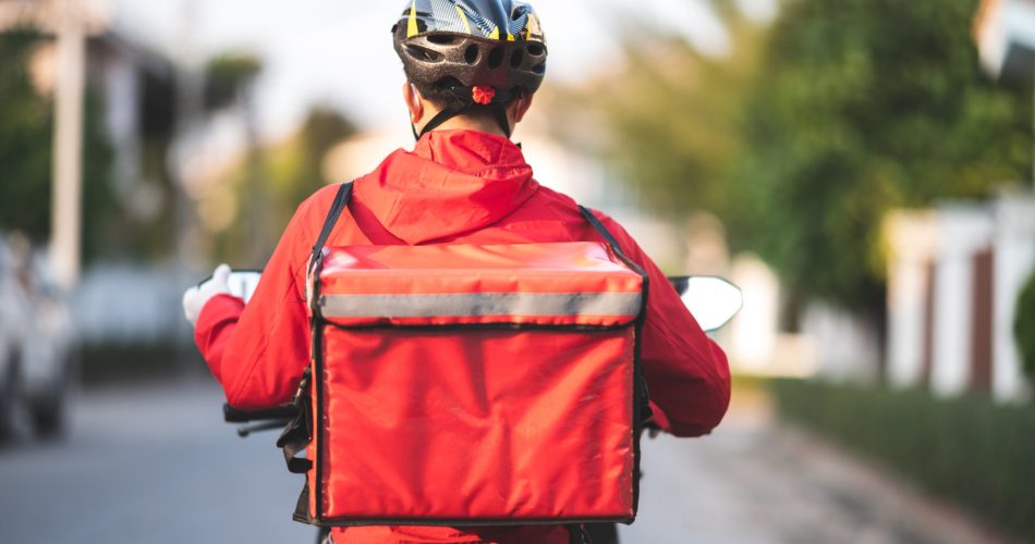 young man working for a food delivery service checking with road motorcycle in the city